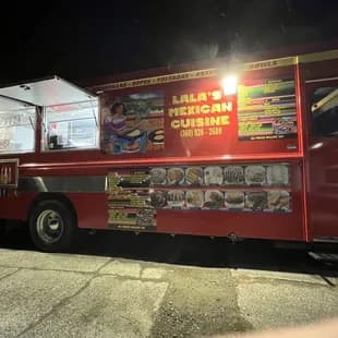 Lala's red food truck at night, its yellow sign glowing in the dark